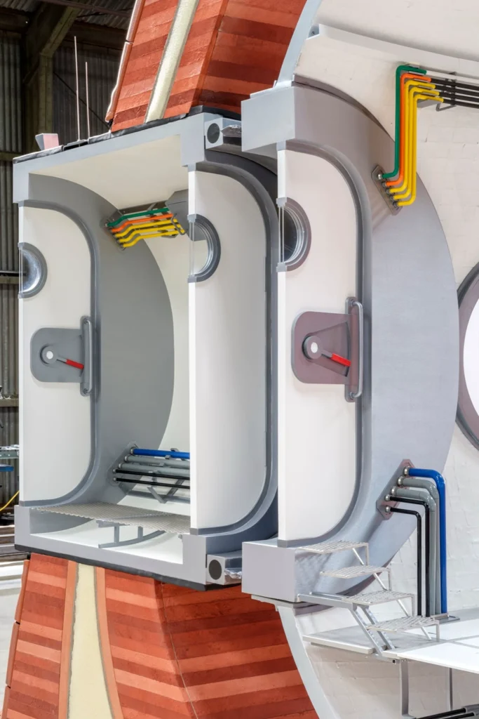 Interior view of a sectional habitat model showing airlock chambers, colourful utility conduits and access steps within a grey and white structure