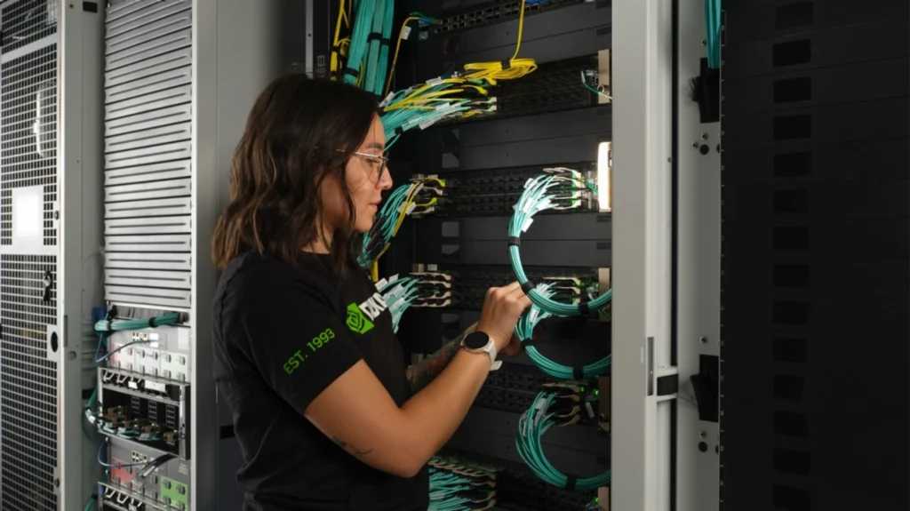 Woman in a black NVIDIA T-shirt carefully managing bundles of teal and yellow fibre cables inside an open server cabinet