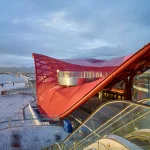 High-angle shot of a red translucent roof canopy with glass escalators and modern station infrastructure visible below.