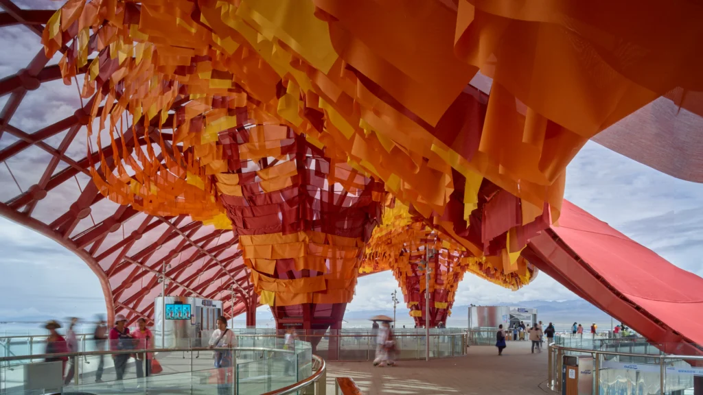 Wide concourse featuring multiple inverted cone structures wrapped in red, orange, and yellow fabric banners under a red canopy.
