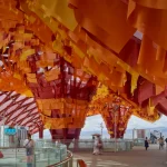 Wide concourse featuring multiple inverted cone structures wrapped in red, orange, and yellow fabric banners under a red canopy.