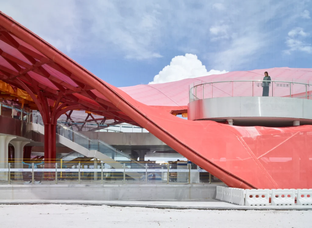 Low-angle view of a red mesh-covered roof swooping down to the platform level near an outdoor staircase and observation platform.