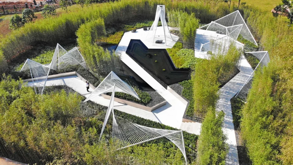 In the Mountains by SSJ Studio: A Picturesque Garden Drawn from Chinese Painting_Aerial view of white geometric steel structures, curved paths and a dark reflecting pool set among dense bamboo