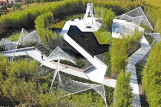 Aerial view of white geometric steel structures, curved paths and a dark reflecting pool set among dense bamboo