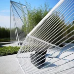 Daytime detail of white steel lattice frames with a dark sculptural stone beneath one structure