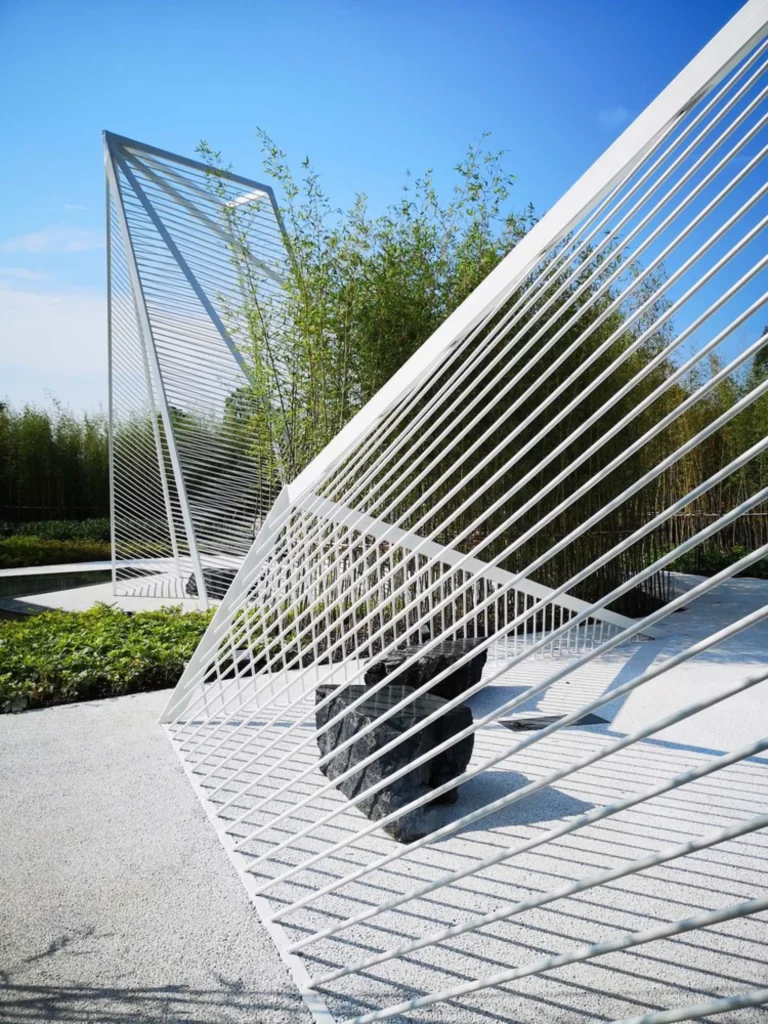 Daytime detail of white steel lattice frames with a dark sculptural stone beneath one structure