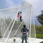 Family interacting with a large white steel climbing structure under a partly cloudy sky