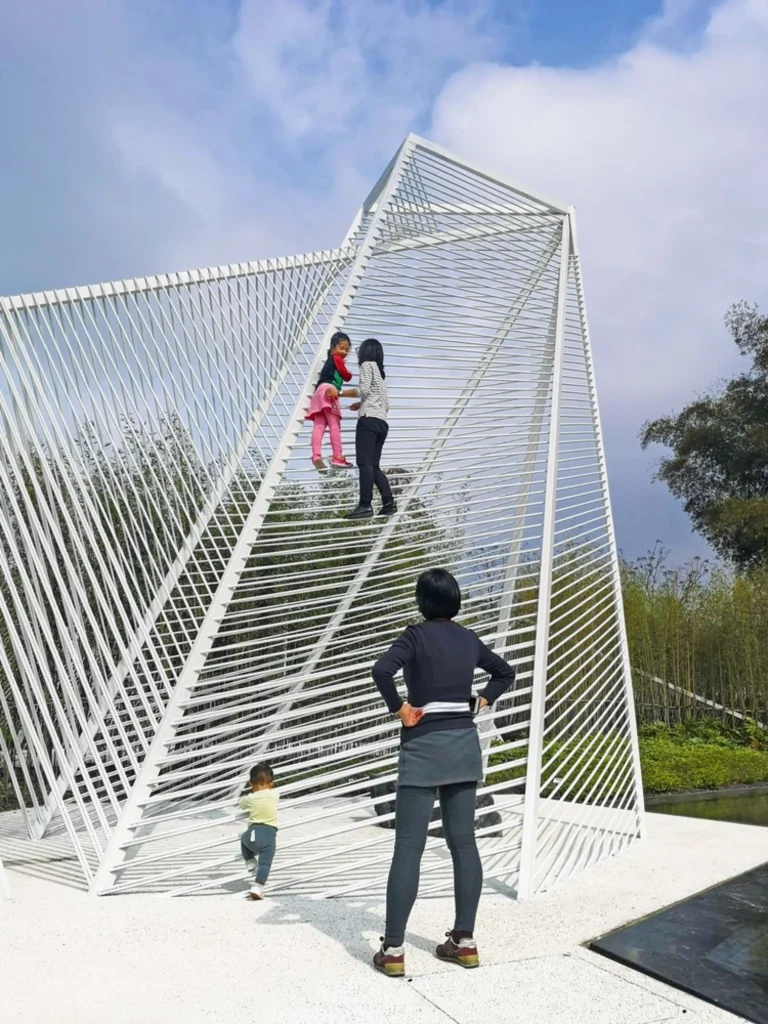 Family interacting with a large white steel climbing structure under a partly cloudy sky
