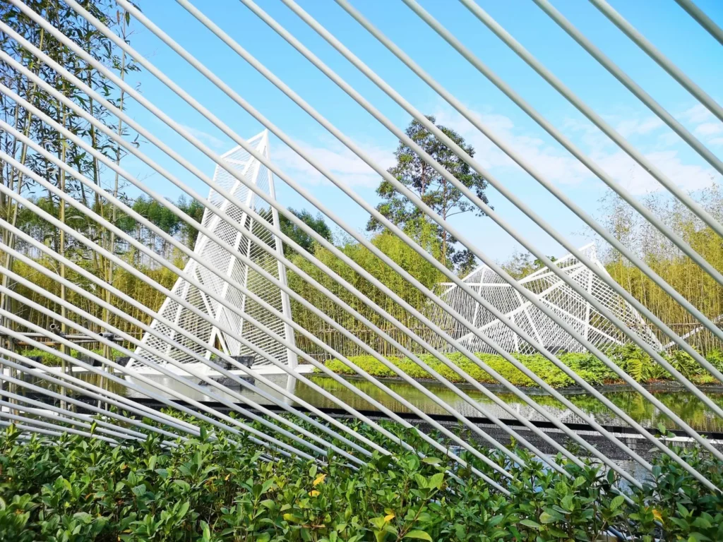 Close view looking through parallel white steel rods toward distant pyramid forms and bamboo