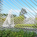 Close view looking through parallel white steel rods toward distant pyramid forms and bamboo