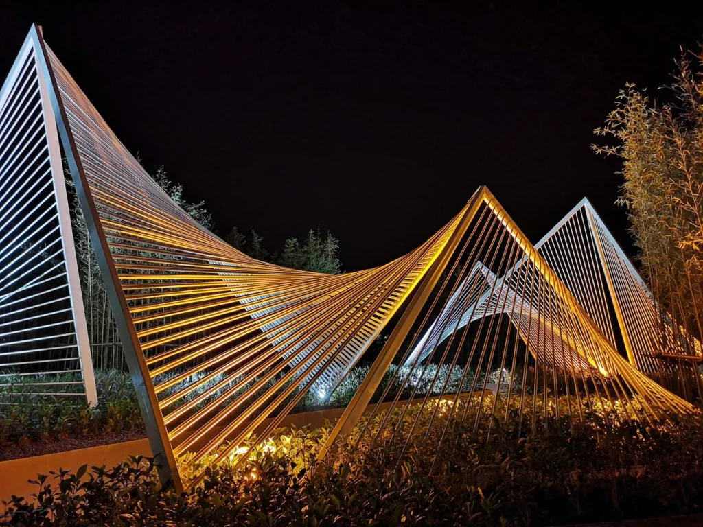 Night close-up of curved and angular white steel frameworks glowing under warm artificial light