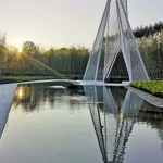 Sunset view of a tall white pyramidal steel structure reflected in a still rectangular pool