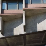 Close-up of the underside of the elevated concrete structure showing deep beams, shadowed recesses and the lower edge of the hotel floors