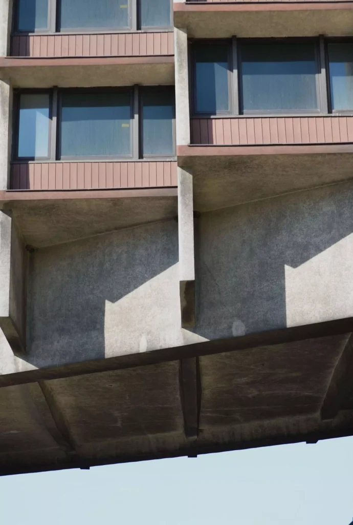 Close-up of the underside of the elevated concrete structure showing deep beams, shadowed recesses and the lower edge of the hotel floors