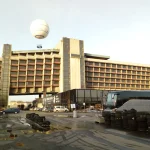 Street-level view of the hotel’s stepped end elevation and long façade, with coaches, parked cars and a large observation balloon overhead