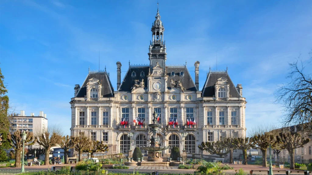 Ornate French town hall building with flags flying under a clear blue sky