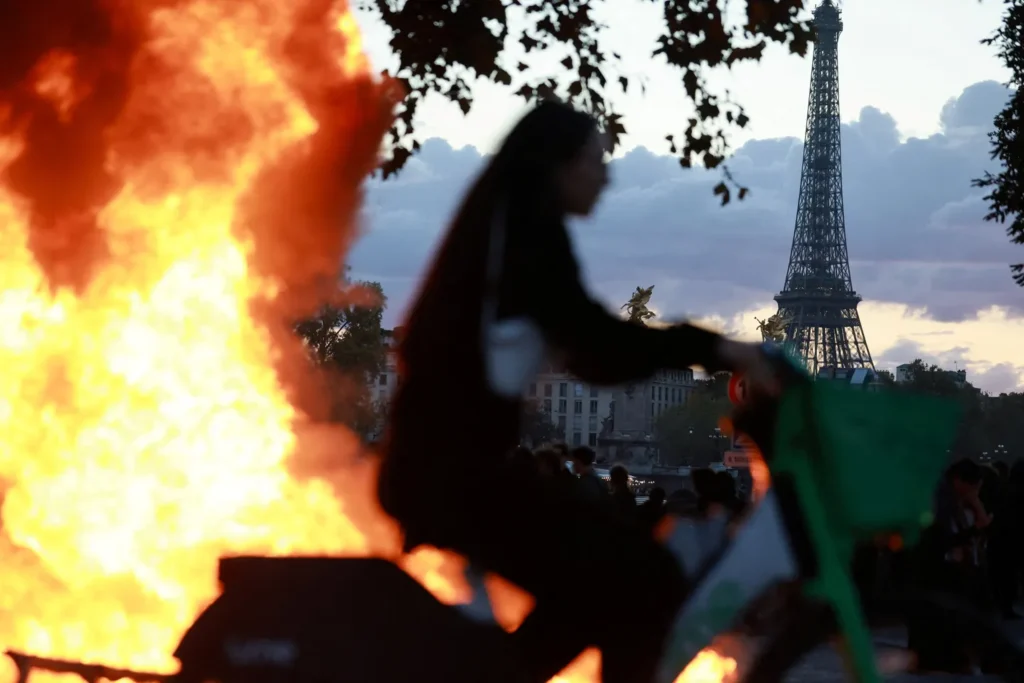 Silhouette of a person on a bicycle against a large fire with the Eiffel Tower visible in the background