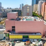 Aerial view of the pink-clad Colburn School expansion under construction amid downtown Los Angeles skyscrapers