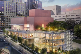 Evening rendering of the illuminated pink and glass building with people on the terrace and dancers visible inside