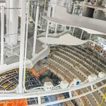 Construction interior showing white structural supports, scaffolding and the curved seating bowl under formation
