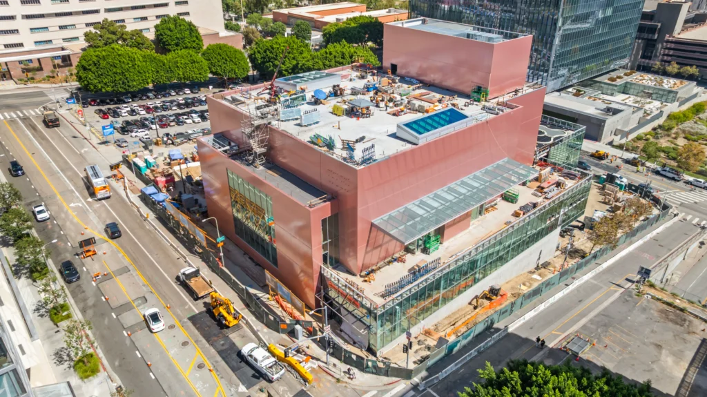 High aerial view of the pink building complex under construction with glass wings and downtown context
