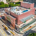 High aerial view of the pink building complex under construction with glass wings and downtown context