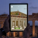 Hands holding tablet displaying 3D augmented reality reconstruction of the ancient Parthenon temple over real ruins at dusk