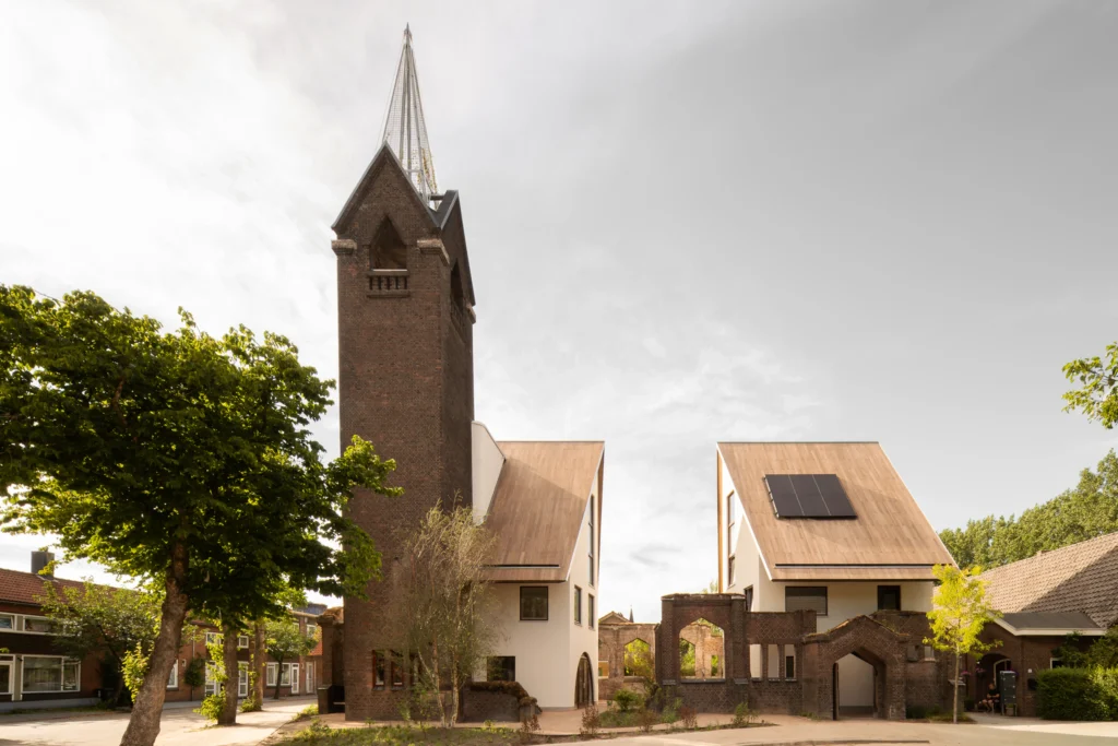 JUUL Exterior view of the rebuilt church tower and two new gabled houses set among remaining brick walls and trees