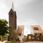 JUUL Exterior view of the rebuilt church tower and two new gabled houses set among remaining brick walls and trees