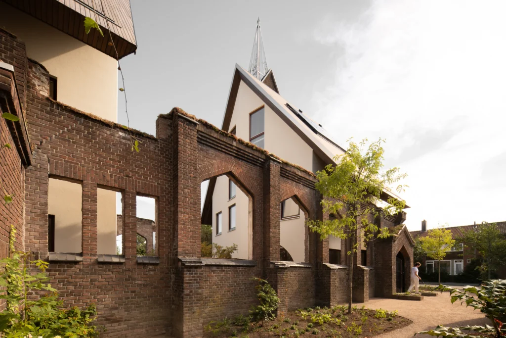 Weathered brick arches of the ruined church frame a view of the new cream-coloured houses with wooden roofs