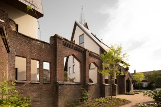 Weathered brick arches of the ruined church frame a view of the new cream-coloured houses with wooden roofs