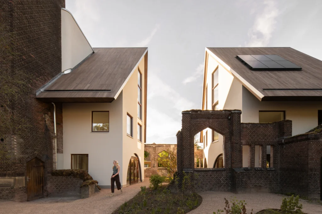 Two modern gabled houses face each other across a gravel courtyard with retained brick arches