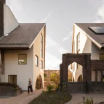 Two modern gabled houses face each other across a gravel courtyard with retained brick arches