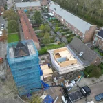 Aerial photograph of the construction site with scaffolding around the tower and timber framing of a new house