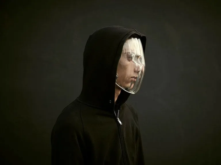 Side profile of a person in a black hoodie wearing a clear, full-face transparent mask