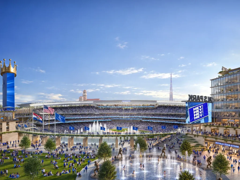 Wide view of the stadium and plaza with crowds, fountains and surrounding mixed-use buildings at dusk