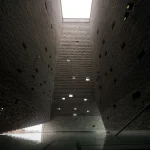 Dramatic upward interior view of a tall brick-lined shaft with scattered square openings and a reflective pool at the base