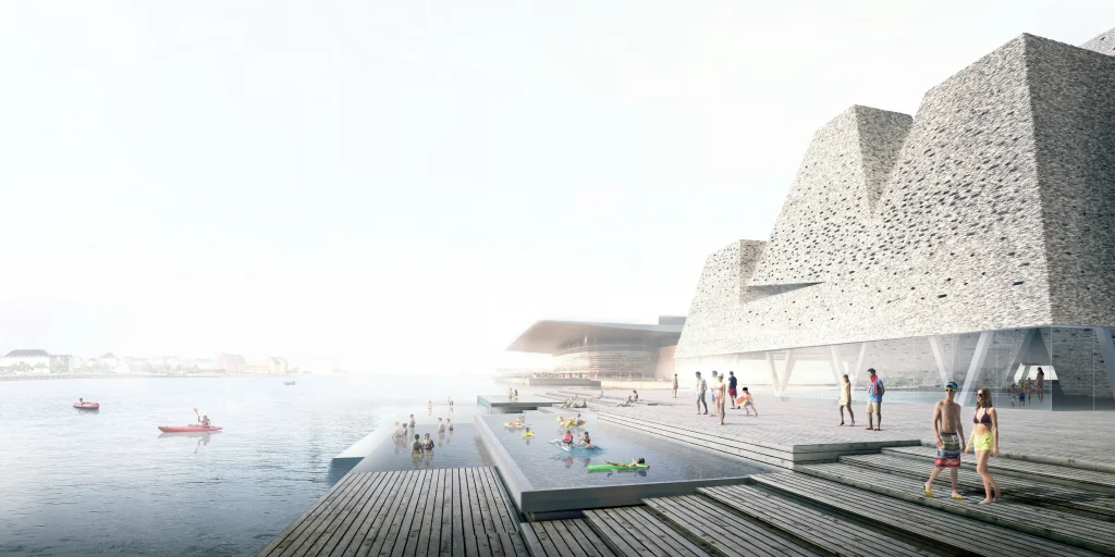Sunny harbour-side scene with people using outdoor pools and wooden decks beside the angular brick building
