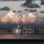 Dramatic evening panorama of the KAI complex and neighbouring buildings across the harbour under a cloudy, colourful sky