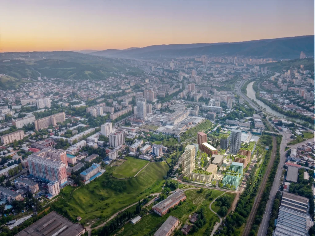 Aerial view of Tbilisi at sunset showing the new Loco Park development with green roofs and varied building colours integrated into the existing urban fabric