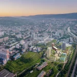 Aerial view of Tbilisi at sunset showing the new Loco Park development with green roofs and varied building colours integrated into the existing urban fabric