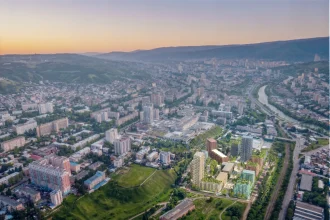Aerial view of Tbilisi at sunset showing the new Loco Park development with green roofs and varied building colours integrated into the existing urban fabric