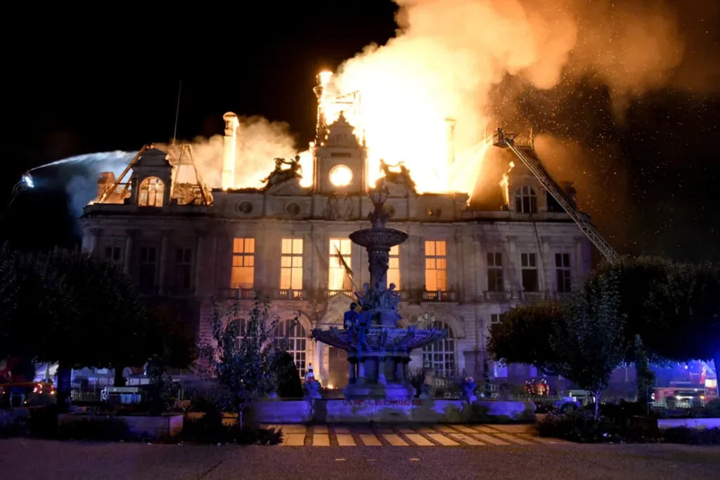 Night view of the town hall fully ablaze with firefighters directing water onto the burning roof and clock tower
