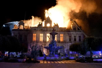 Night view of the town hall fully ablaze with firefighters directing water onto the burning roof and clock tower