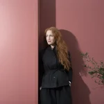 Portrait of architect Mary Duggan standing against a yellow brick wall