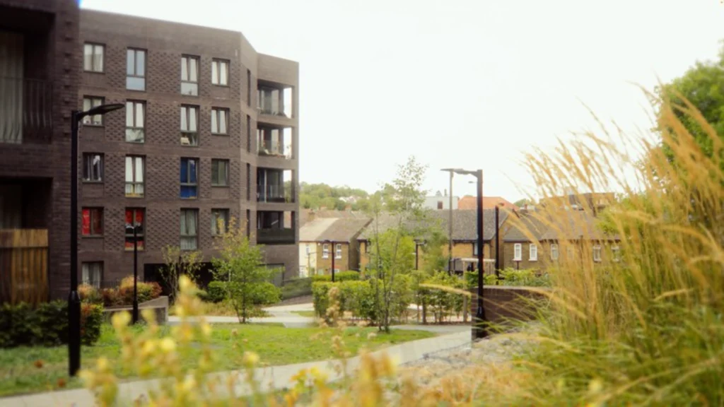View through planting toward one of the dark brick pavilion blocks with balconies and street lighting