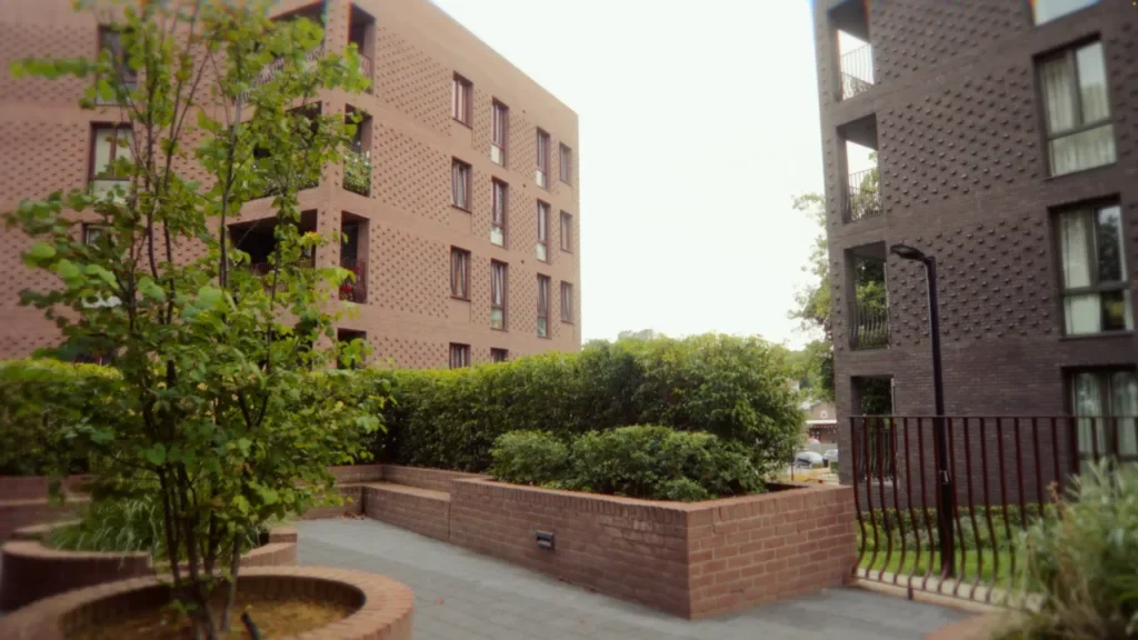 Courtyard space between two textured brick buildings with raised planters and hedging