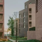 Pathway winding between the brick facades with young trees and planting beds