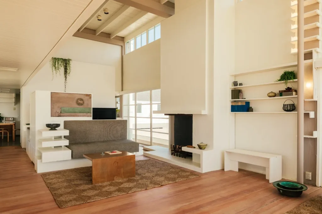 Living room interior with built-in white shelving, grey sofa, wooden coffee table and a tall white fireplace under a sloped ceiling