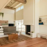 Living room interior with built-in white shelving, grey sofa, wooden coffee table and a tall white fireplace under a sloped ceiling
